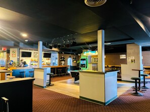 A bar area with stools, a counter, and a neon sign.