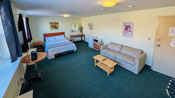 Habitación de hotel con cama, sofá, mesita pequeña, escritorio, televisor y puerta.