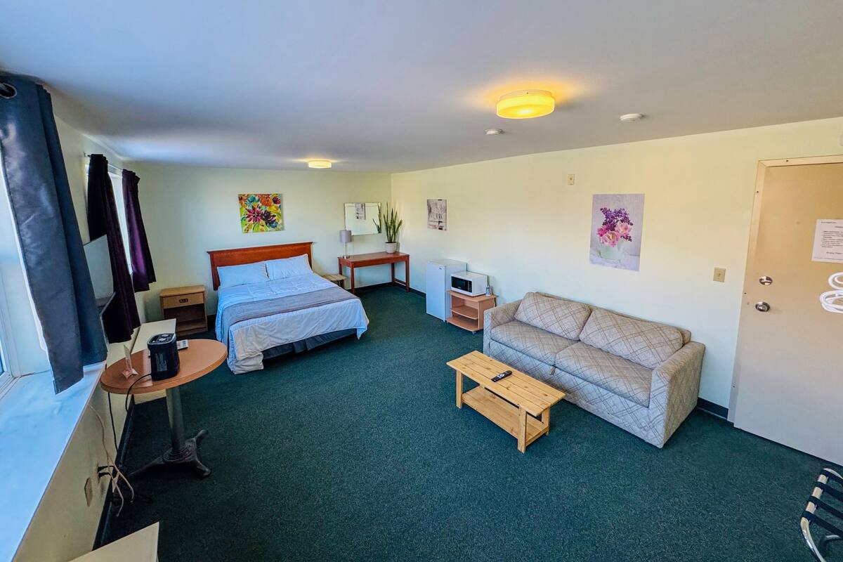 Ein Hotelzimmer mit Bett, Sofa, einem kleinen Tisch, Schreibtisch, Fernseher und einer Tür.