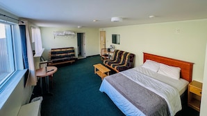 A hotel room with a bed, a sofa, a small table, a chair, a desk, a mirror, and a window. - Asessippi Inn (Russell)