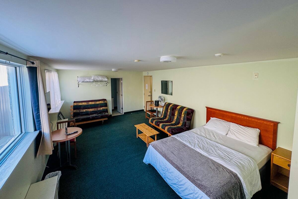 Ein Hotelzimmer mit einem Bett, einem Sofa, einem kleinen Tisch, einem Sessel, einem Schreibtisch, einem Spiegel und einem Fenster.