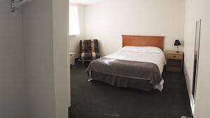 A hotel room with a bed, a nightstand, a chair, a lamp, and a wardrobe. - Asessippi Inn (Russell)