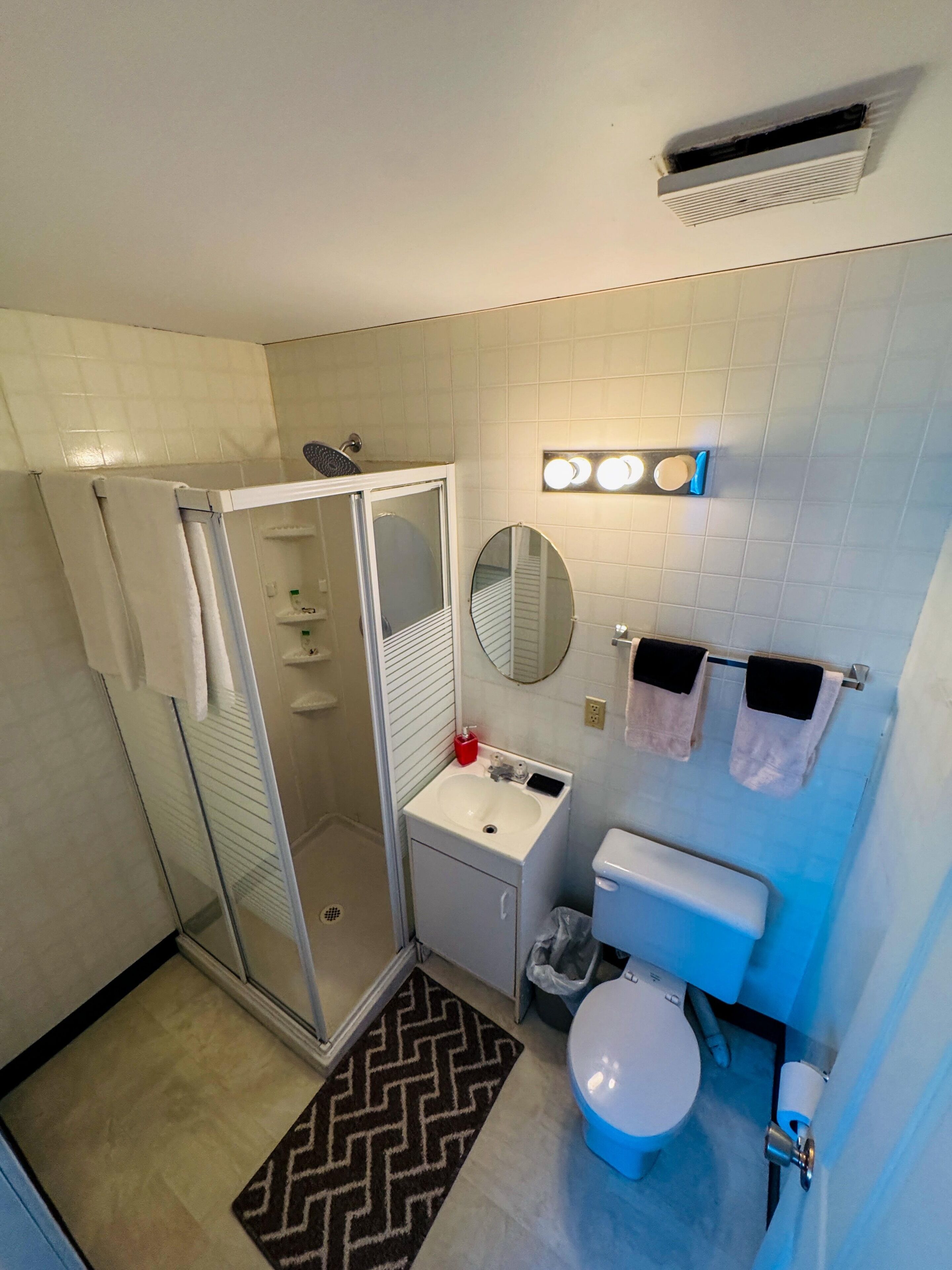 Une salle de bain compacte avec une douche à parois de verre, un lavabo blanc, des toilettes et un miroir.