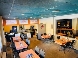 A restaurant with tables and chairs, a counter with a menu, and a kitchen area.