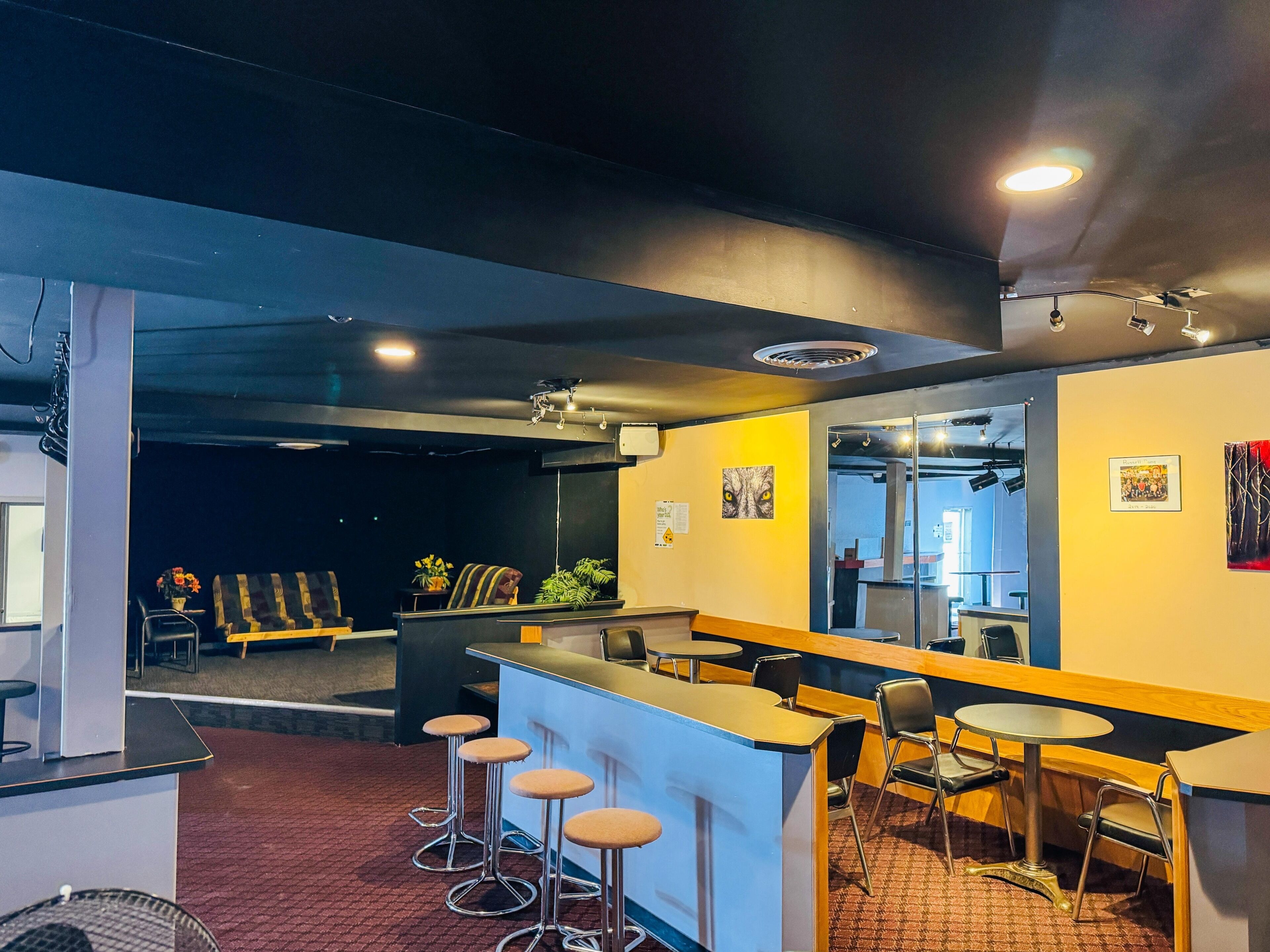 Zona de bar con taburetes, una barra y un área de estar con mesas y sillas.