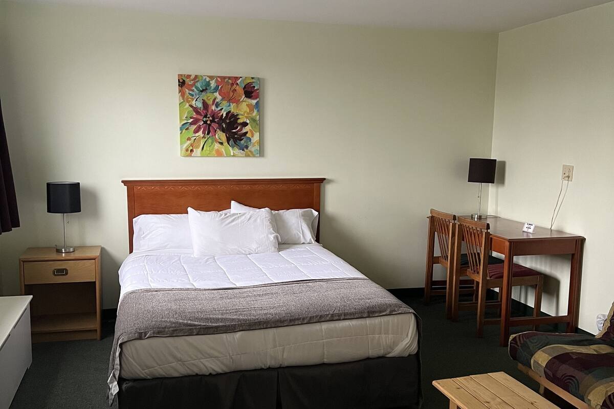 Ein Hotelzimmer mit Bett, Nachttisch, Schreibtisch, Stuhl und einem Gemälde an der Wand.
