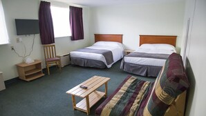 A hotel room with two single beds, a sofa, a small wooden table, a chair, a TV mounted on the wall, and a window with curtains. - Asessippi Inn (Russell)