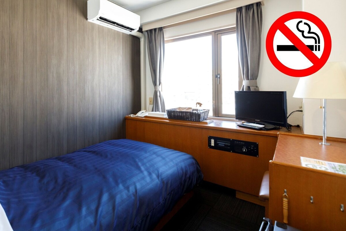 Una habitación de hotel con cama, escritorio, computadora, televisor y aire acondicionado.
