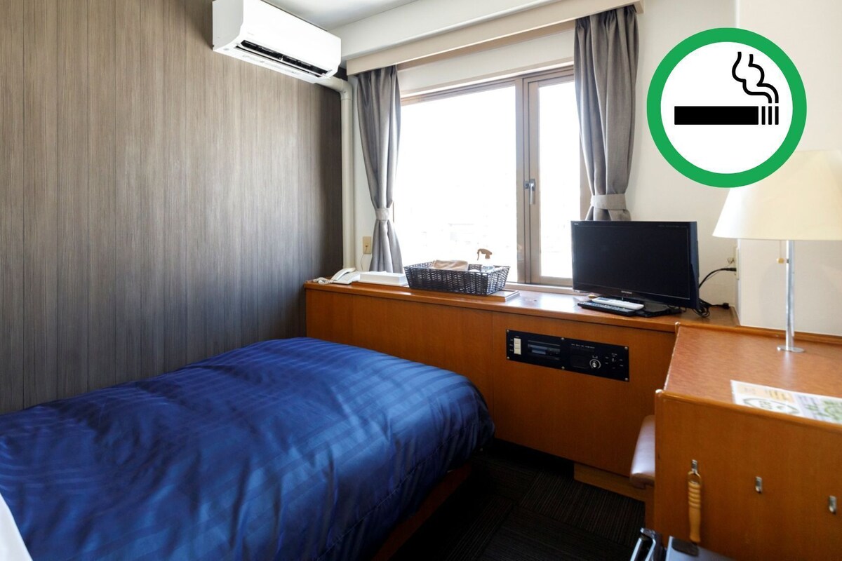 Habitación de hotel con cama, escritorio con ordenador, aire acondicionado y ventana con cortinas.