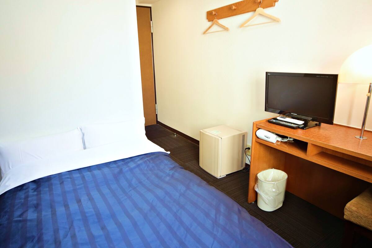 Quarto de hotel com cama, escrivaninha com televisão, aquecedor e lixeira.