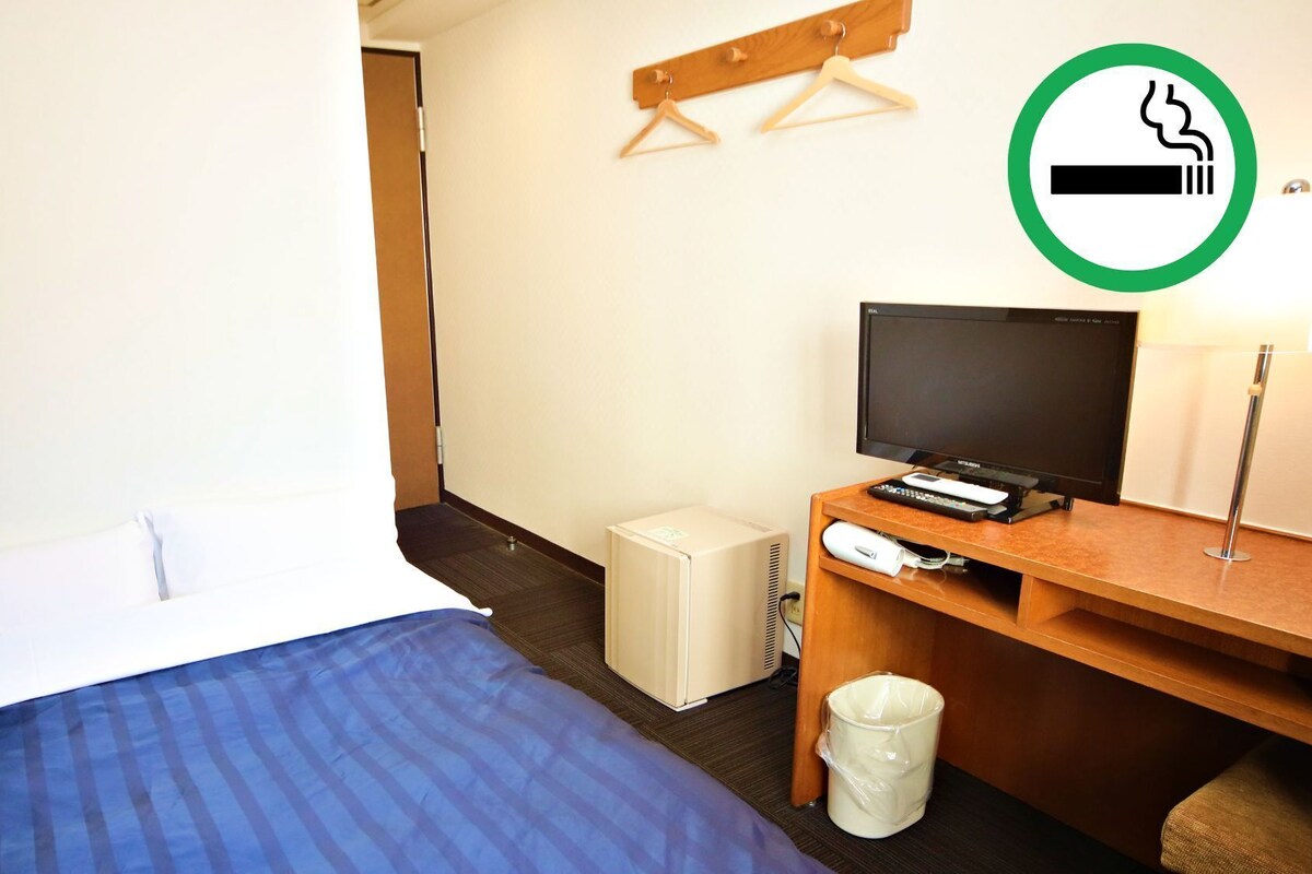 Habitación de hotel con cama, escritorio con televisor, calentador pequeño y cartel de no fumar.