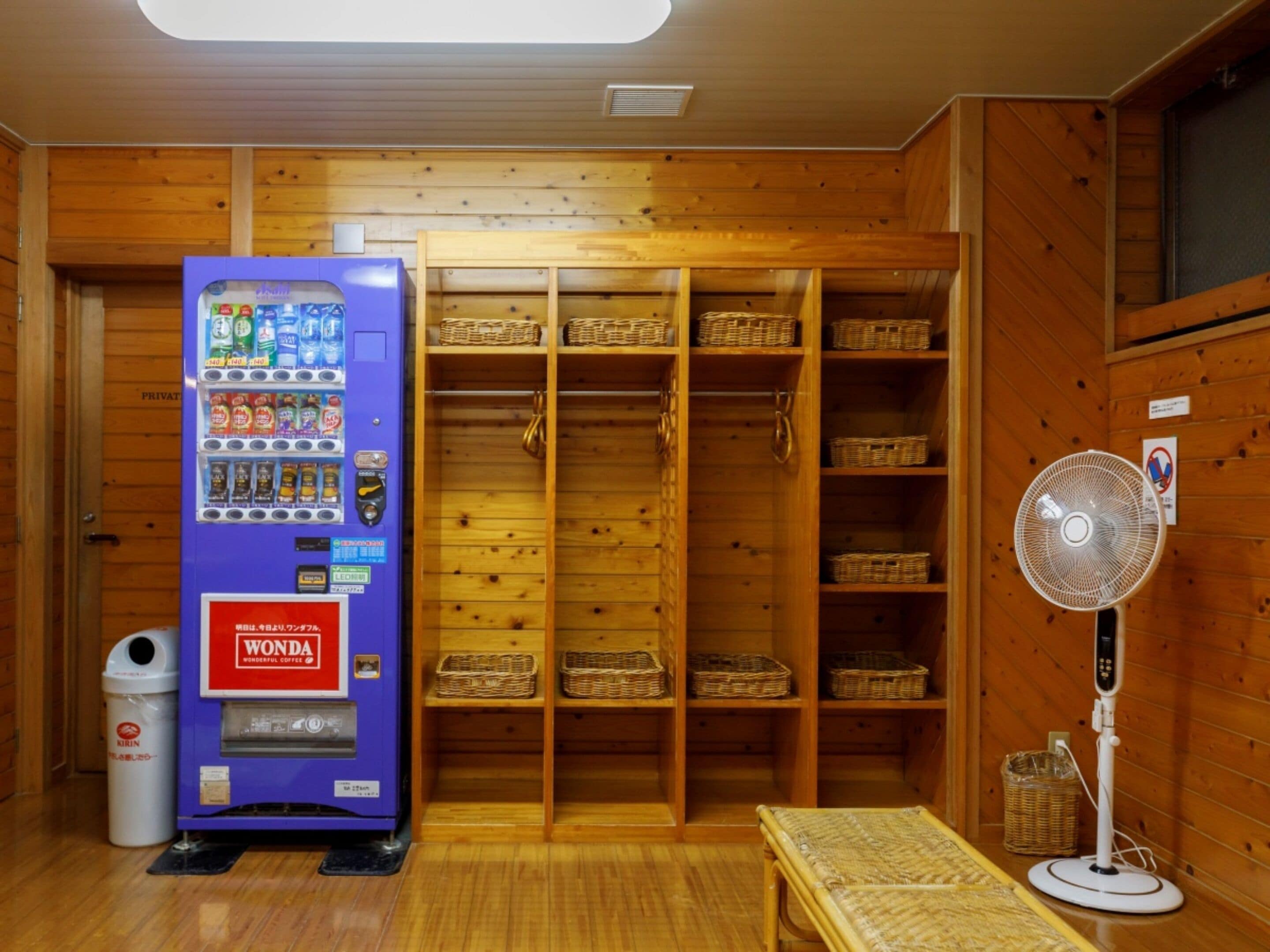 A room with a vending machine, wooden shelves, and a fan.