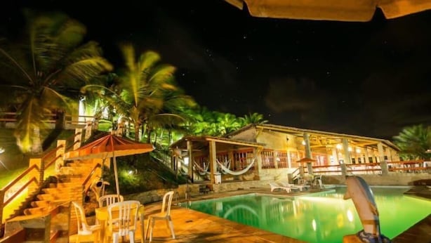 Zona de piscina nocturna con una escalera de piedra, sillas de descanso y una hamaca.