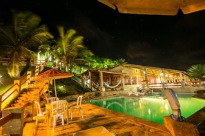 A nighttime pool area with a stone staircase, lounge chairs, and a hammock. - Chalemar Hotel Pousada (Baia Formosa)