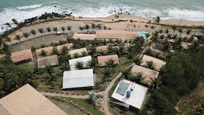 Vista aérea de un complejo turístico con varias edificaciones tipo bungalow, una playa y un litoral rocoso.