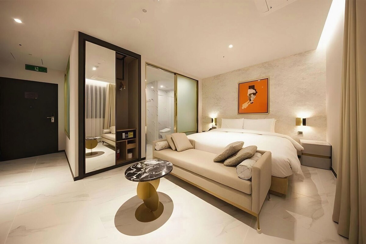A modern hotel room with a large bed, a sofa, a small table, and a mirror.