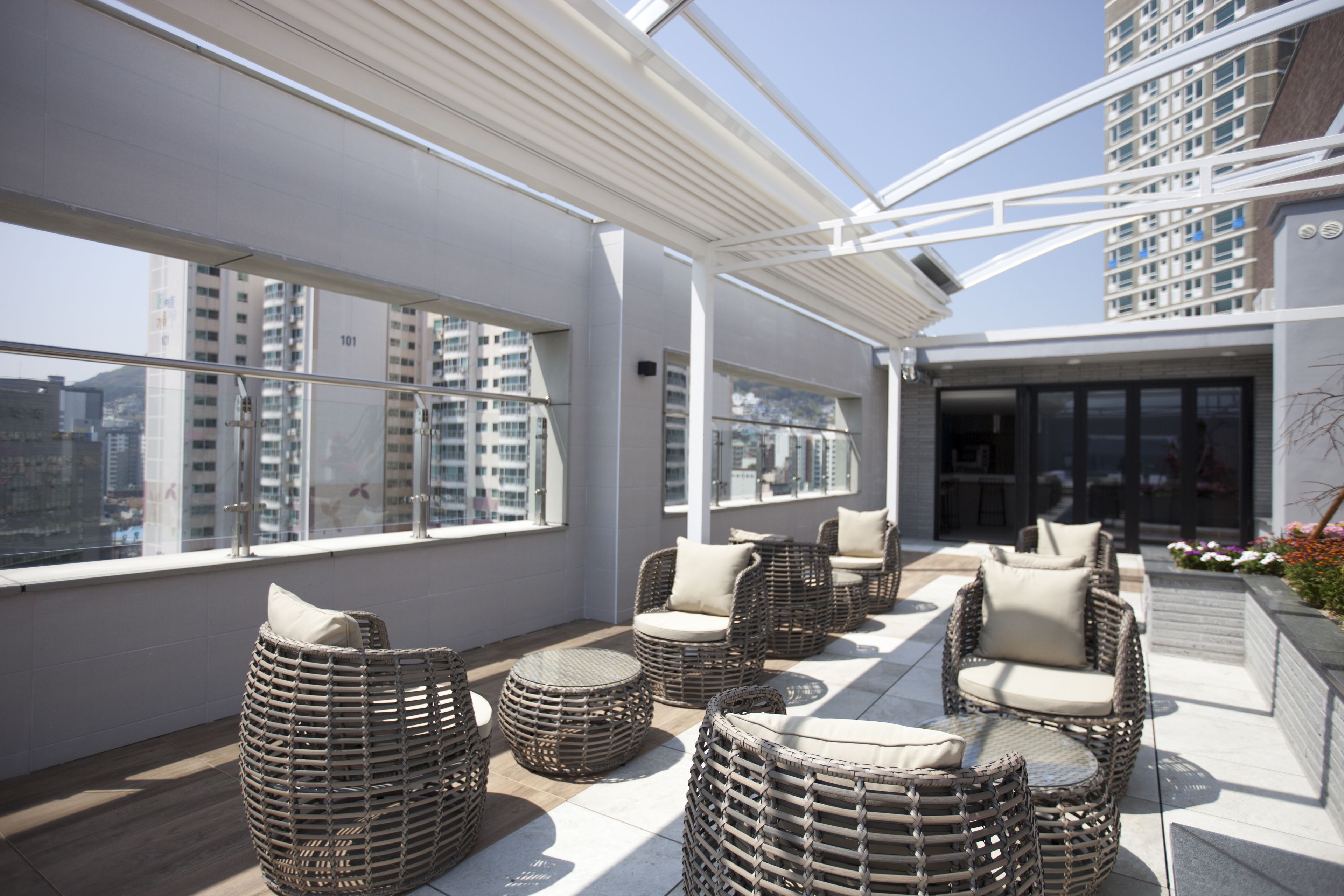 A rooftop terrace with wicker furniture, large windows, and a view of high-rise buildings.