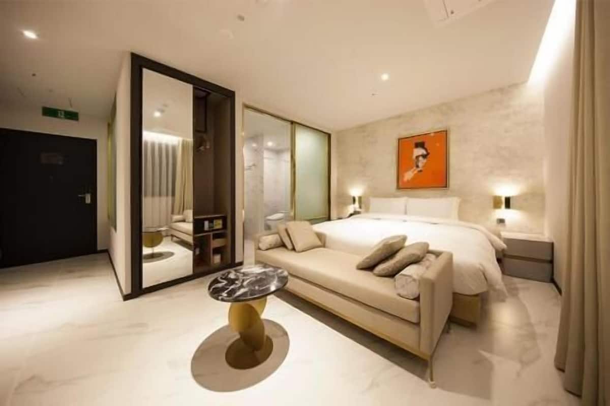 A modern hotel room with a large bed, a sofa, a small round table, and a mirror.