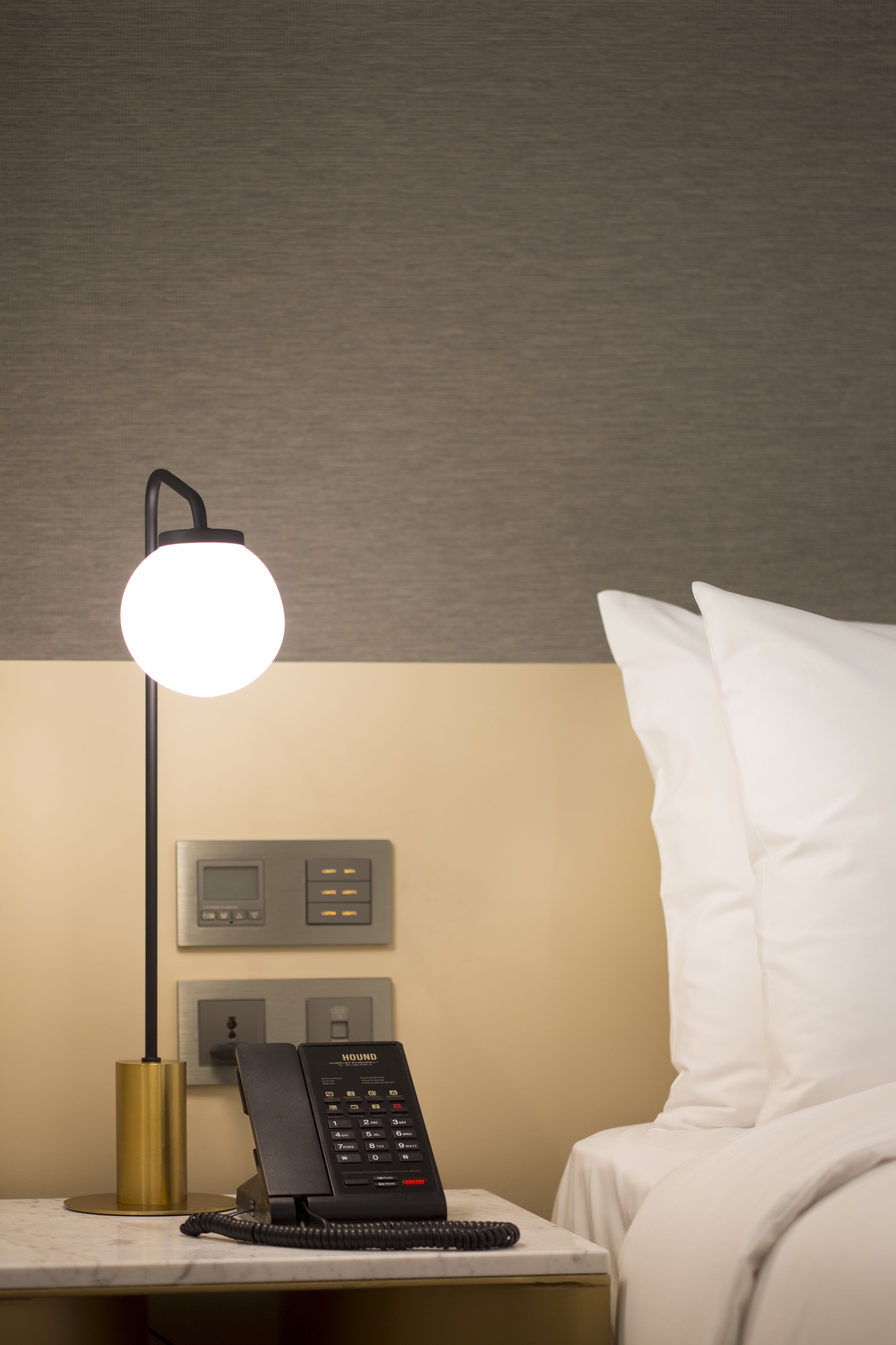 Une chambre d’hôtel avec une table de chevet, un téléphone noir, une lampe et un lit avec des oreillers blancs.
