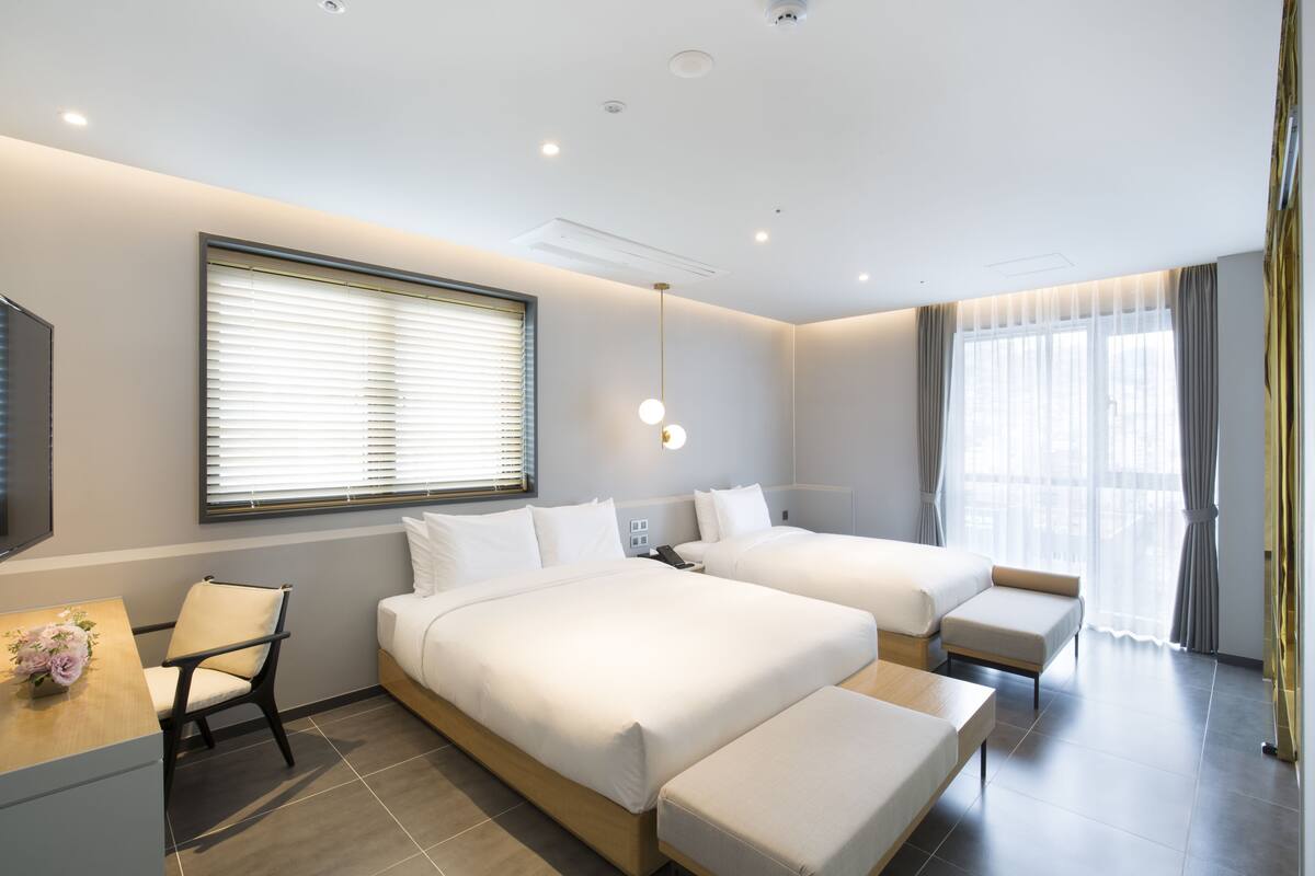 A modern hotel room with two beds, a desk, and a chair.