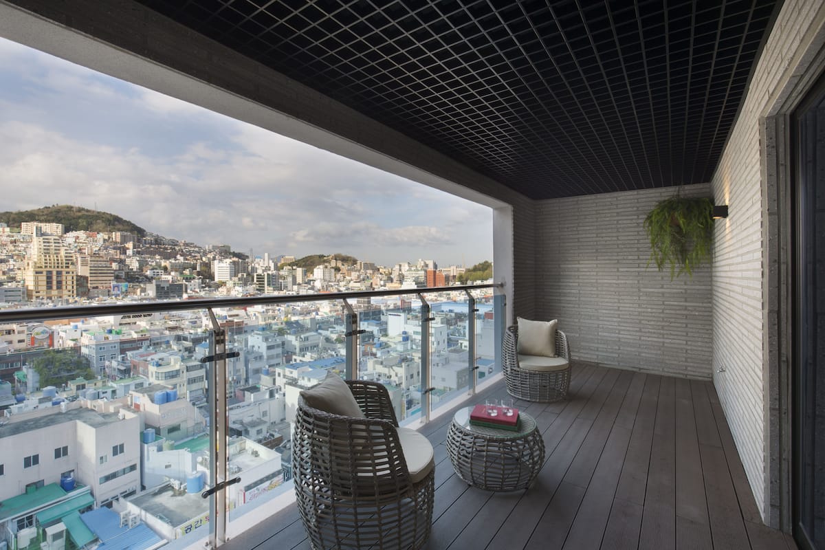 A balcony with wicker furniture, a hanging plant, and a city view.