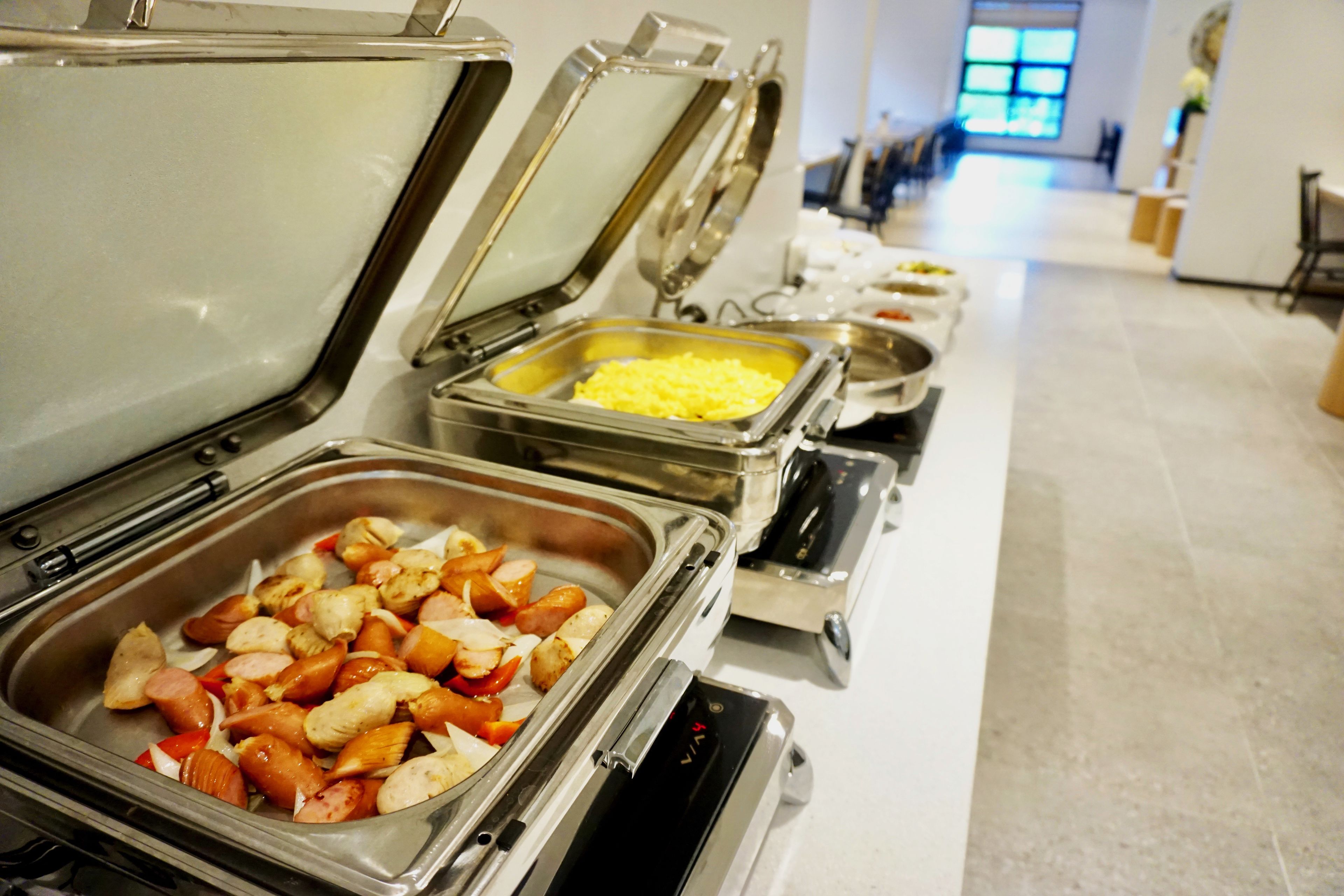 Un bufé con diversos alimentos en recipientes de acero inoxidable, incluyendo carnes y quesos.