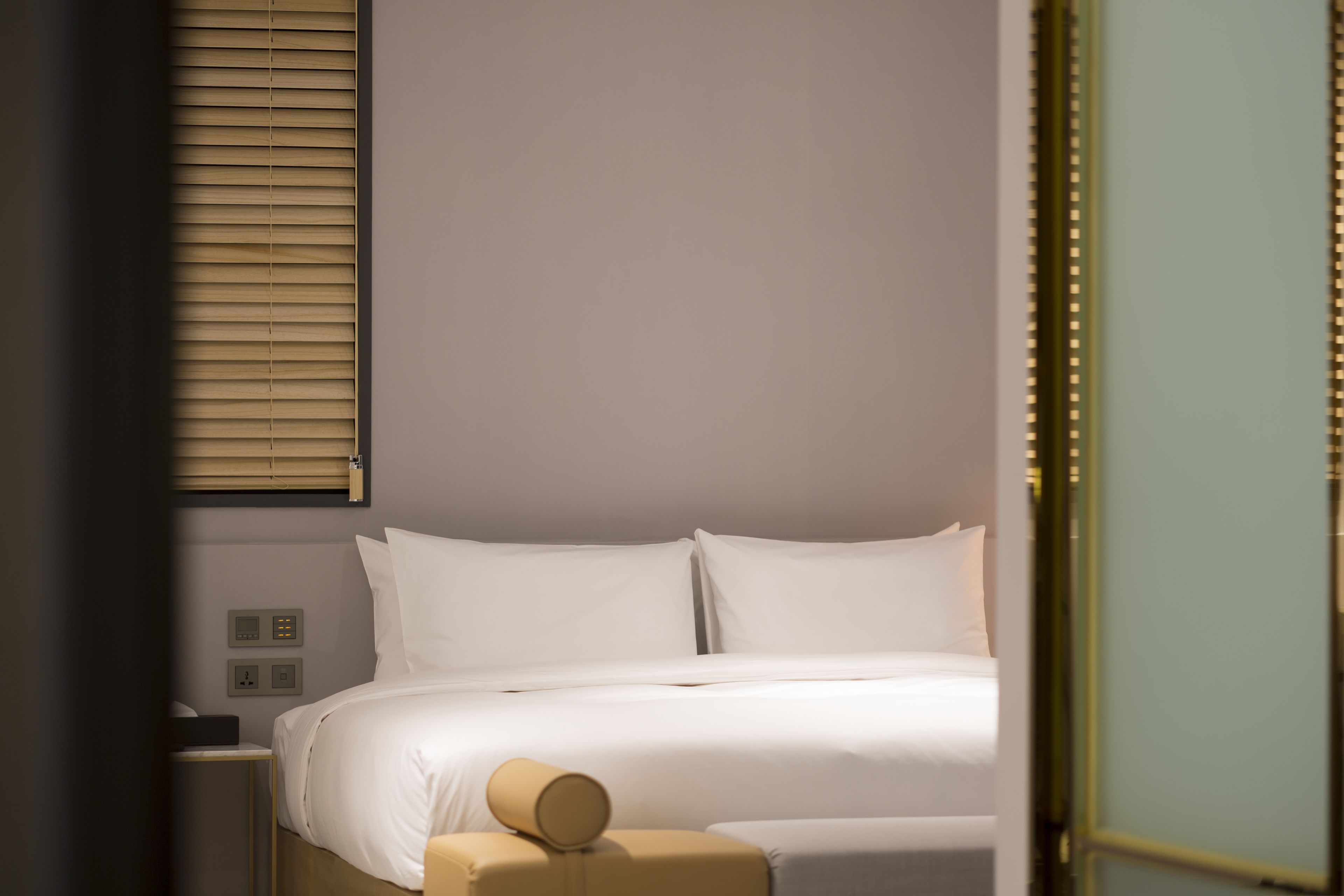 A hotel room with a bed, a bedside table, and a wall-mounted control panel.