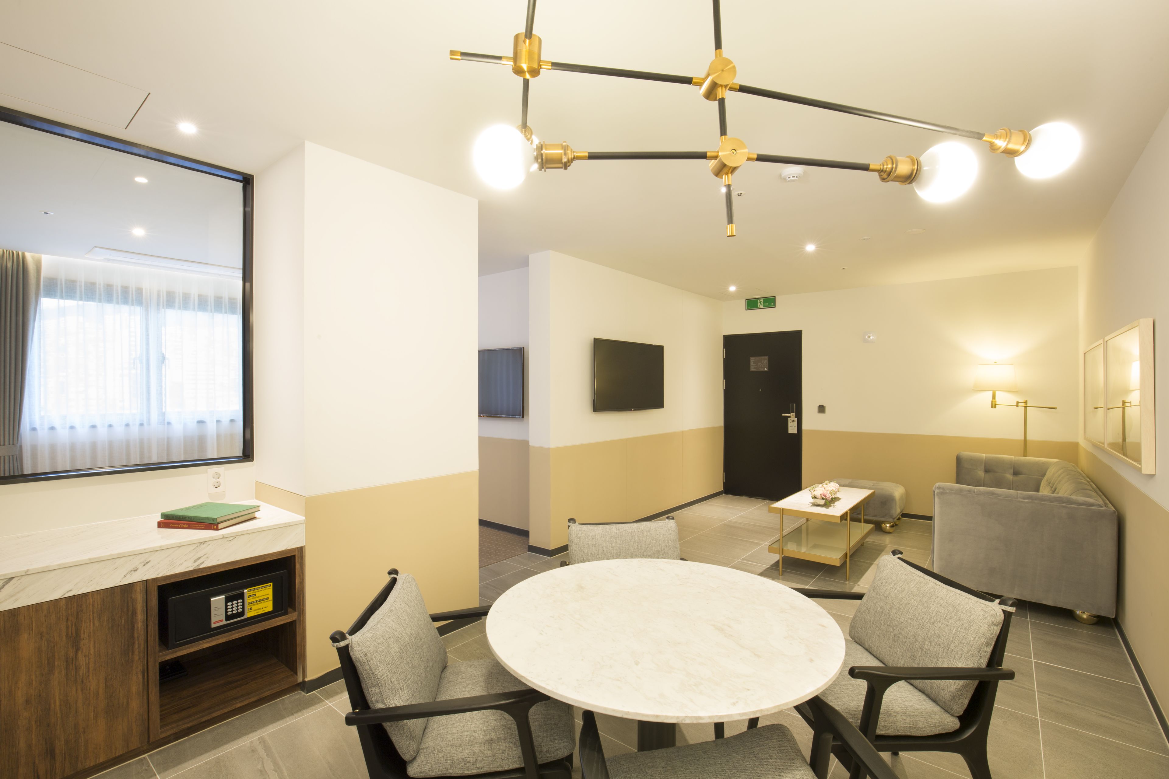 A hotel lobby with a round table, chairs, a reception desk, a television, and a sofa.