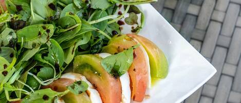 A plate of fresh salad with greens and tomatoes, a bottle of Heineken beer, and a glass of water on a brick table.
