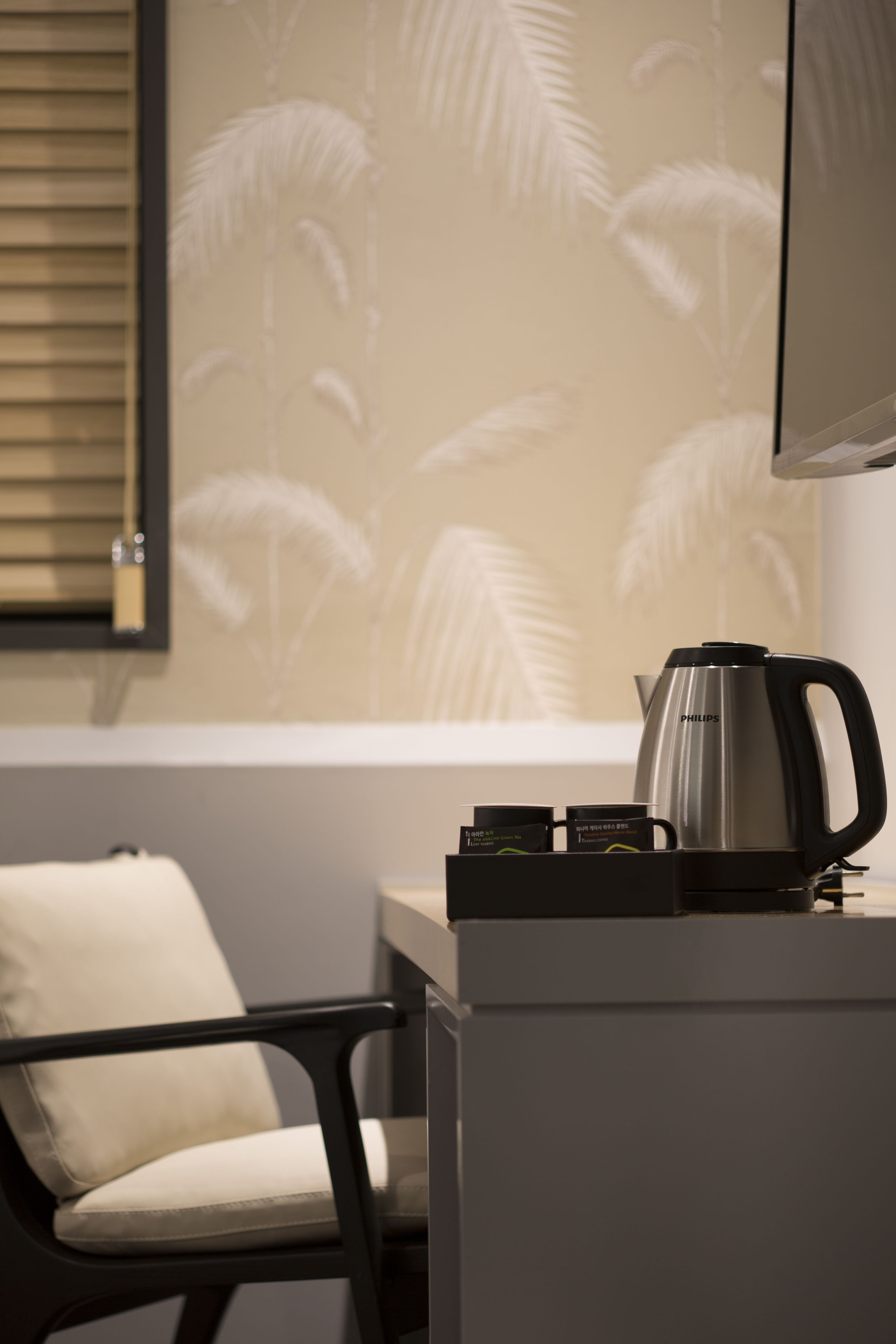 Una habitación moderna con cafetera, una silla y un muro con motivos de hojas de palma.