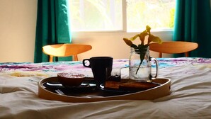 Ein Frühstücksbrett mit einem Muffin, einer schwarzen Tasse und einem Glas Wasser auf einem Bett mit einer blumigen Tagesdecke.