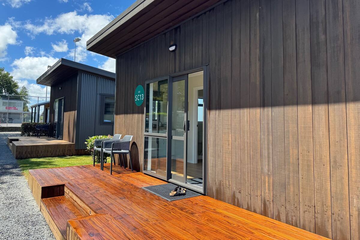 A modern building with a wooden exterior, a covered outdoor seating area with a table and chairs, and a sign indicating an eco-friendly location.