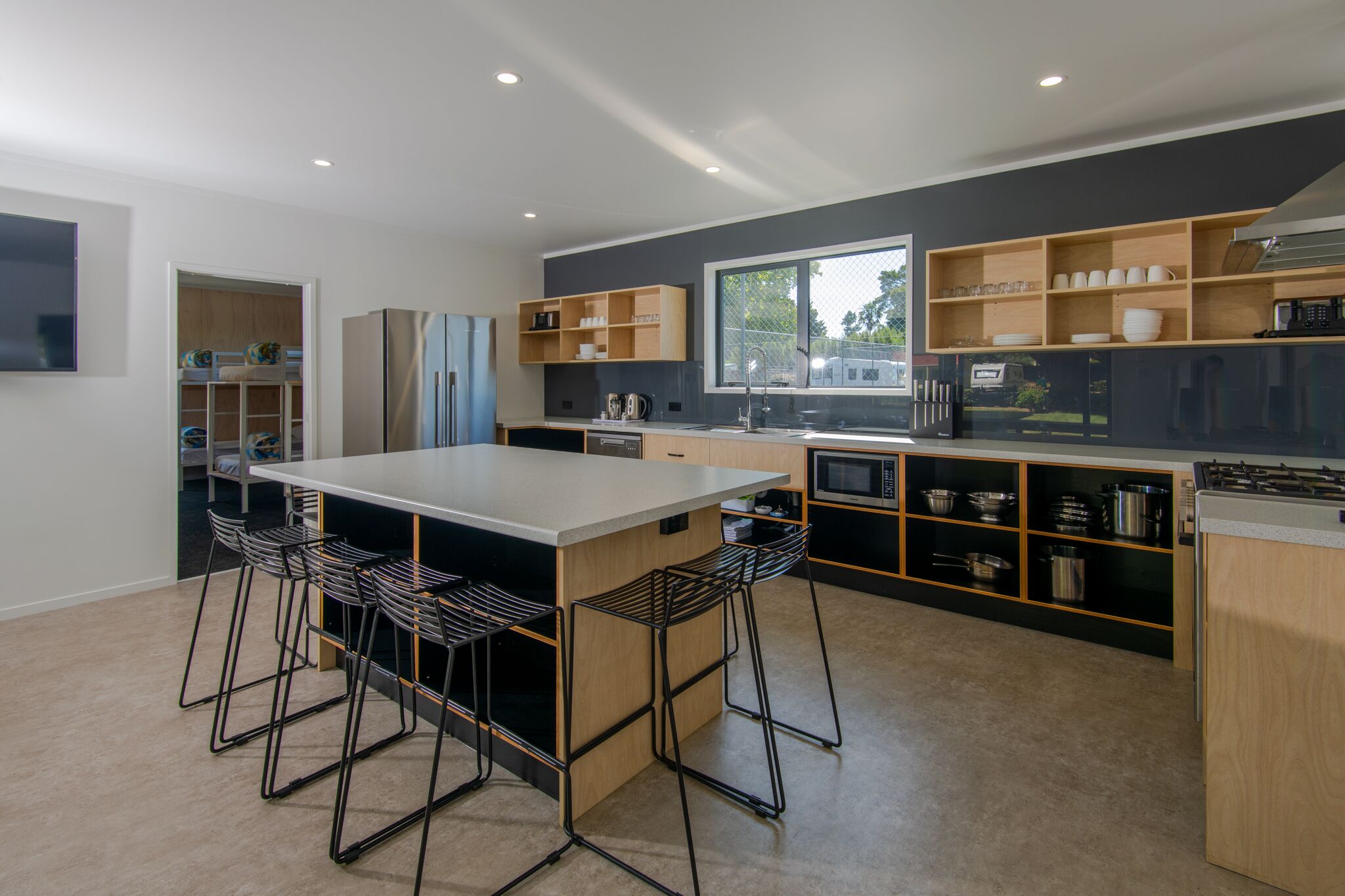 A modern kitchen with a central island, bar stools, built-in shelves, and a large window.