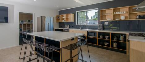 A modern kitchen with a central island, bar stools, built-in shelves, and a large window.
