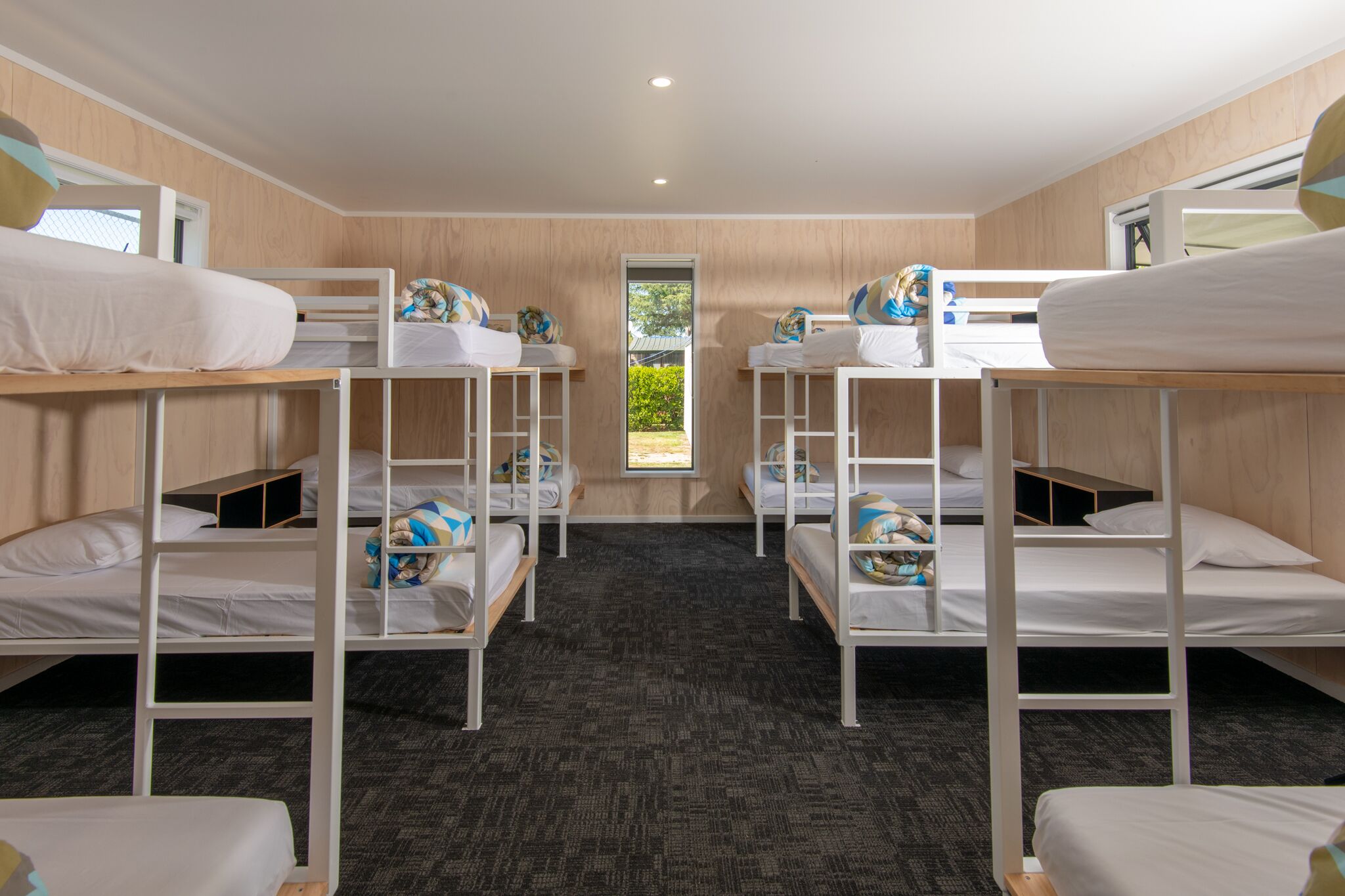A room with bunk beds, a carpeted floor, and a window with a view of greenery.