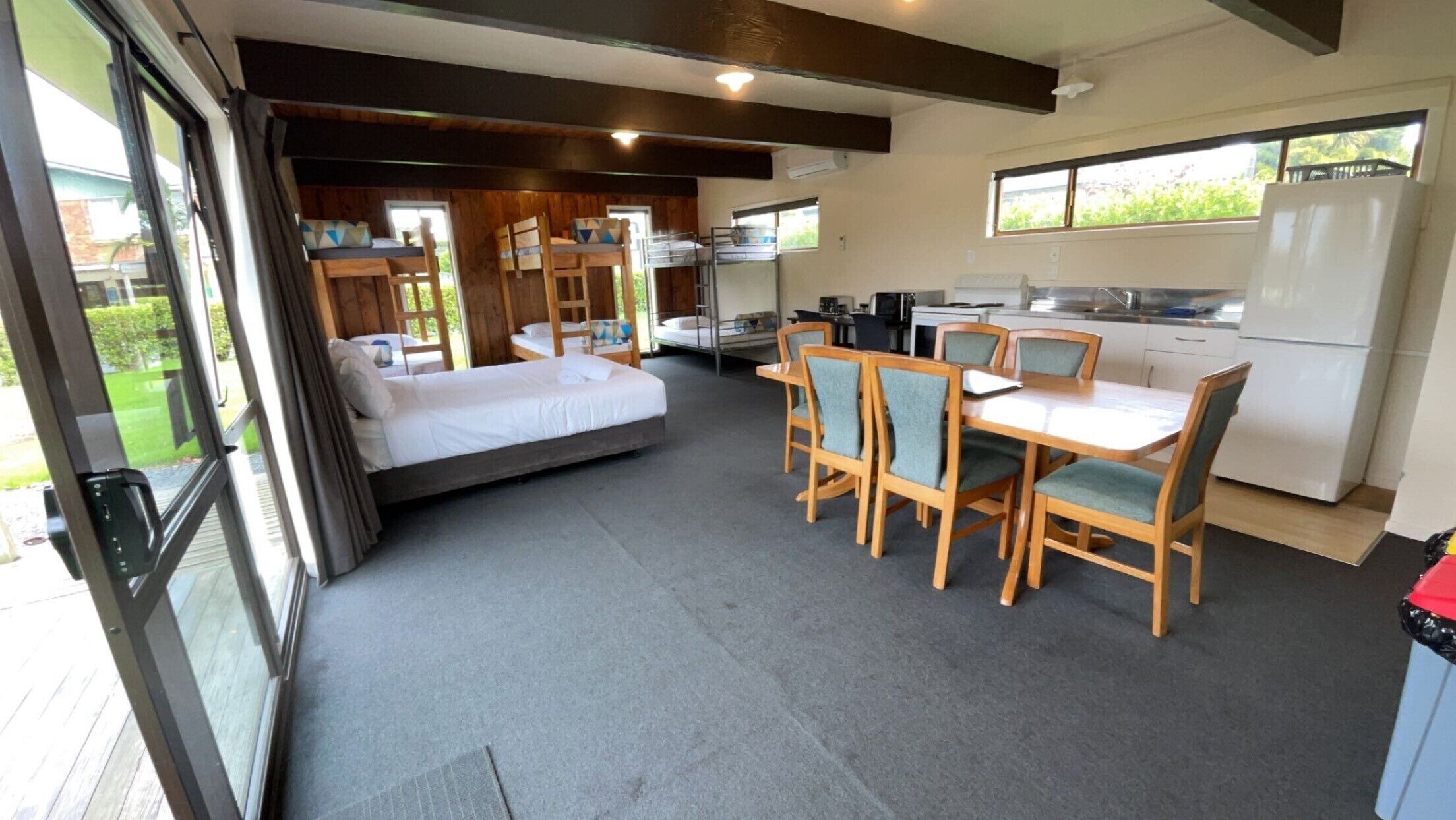 A compact, modern room with a bed, a dining table with chairs, a kitchen area, and a large window providing natural light.