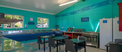 A kitchen with teal walls, stainless steel appliances, and a glass counter. There are four chairs and a table.