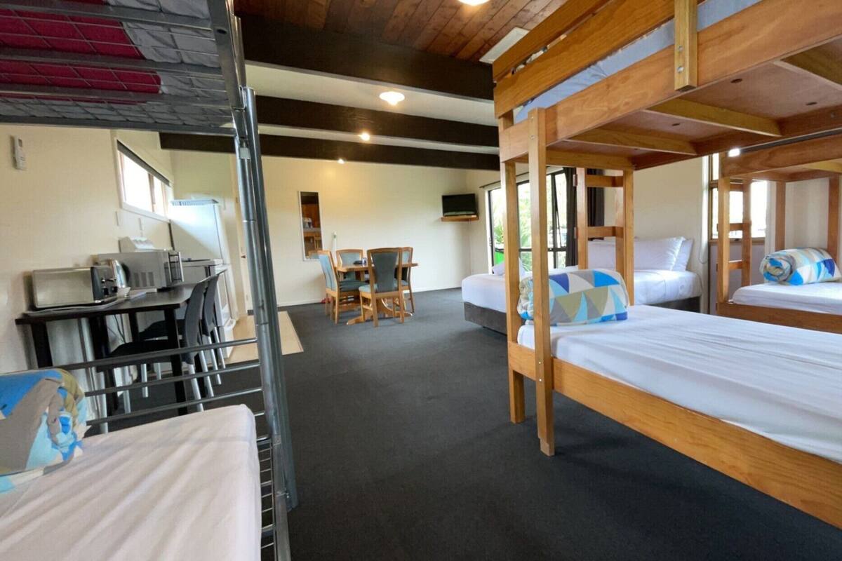 A bunk bed room with a desk and chairs, a television, and a window.