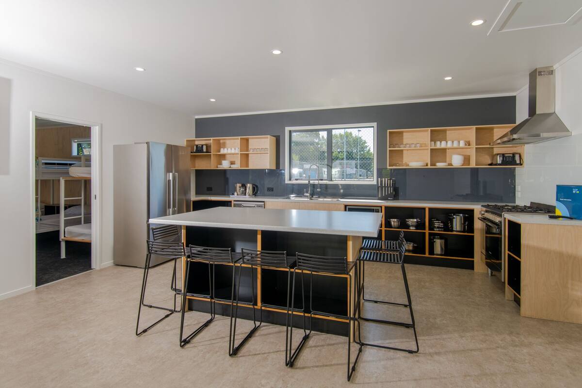 A modern kitchen with a central island, bar stools, built-in shelves, and a view of the outdoors.