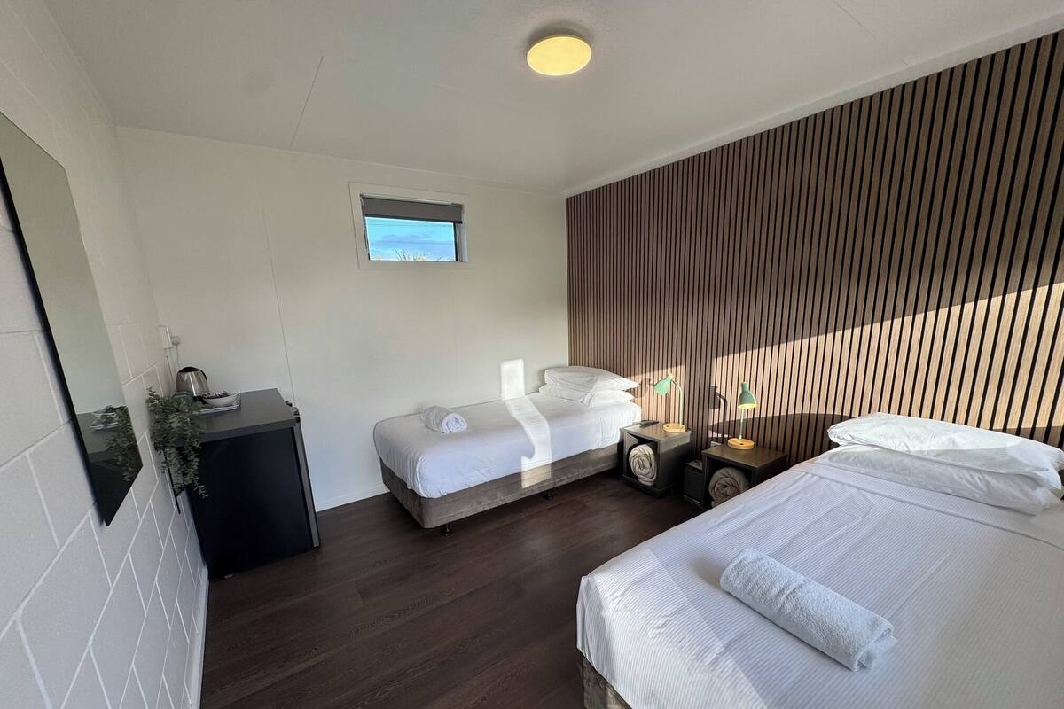 A hotel room with a bed, a bedside table, a small desk, and a window.
