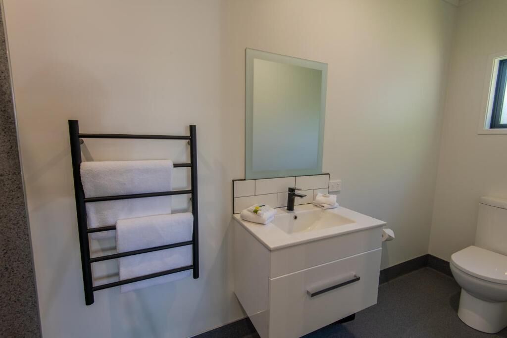 A bathroom with a white sink, a mirror, a black towel rack, and a toilet.