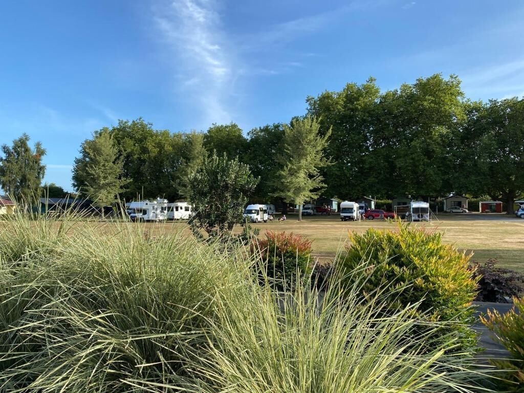 Un camping con vehículos recreativos y tiendas de campaña, rodeado de árboles y zonas verdes.