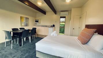 Una habitación de hotel con cama, escritorio con sillas, kitchenette y ventana.