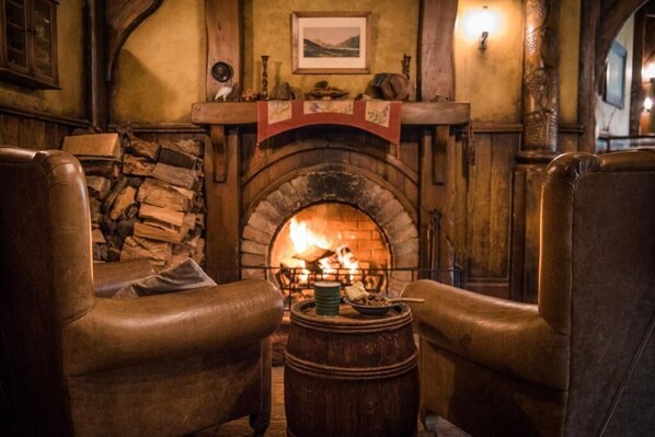 Una habitación acogedora con chimenea de piedra, sillones de cuero y un barril de madera.