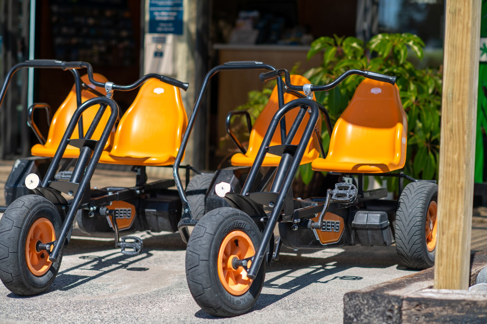 Trois chariots de service orange, dotés de châssis et de roues noirs, sont stationnés à l’extérieur.