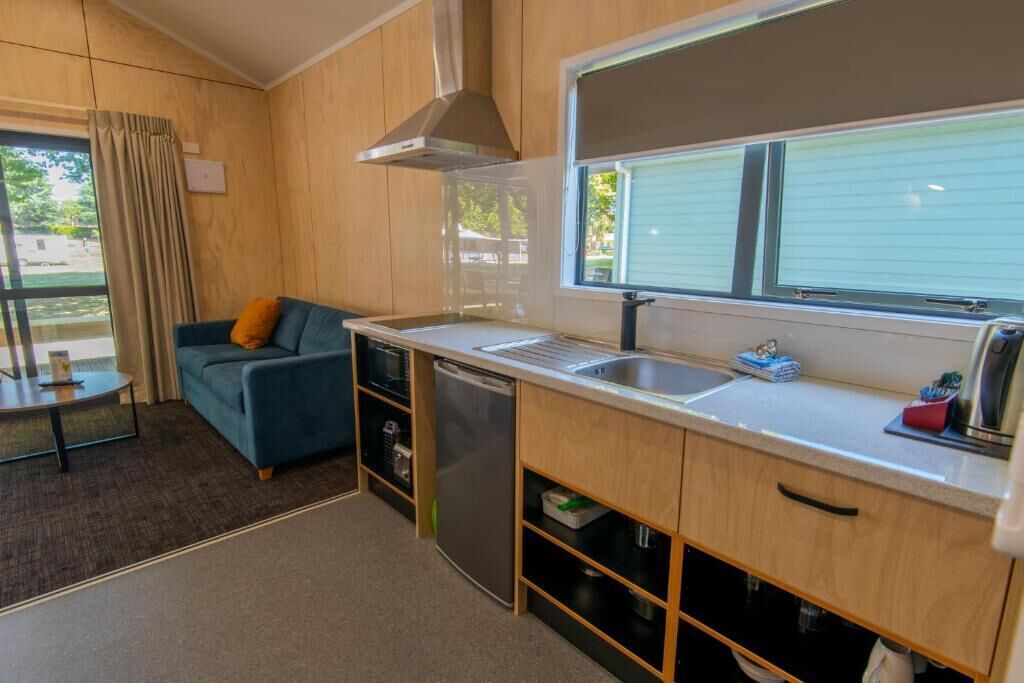 A compact kitchen with a built-in dishwasher, a sink, and a window with blinds.