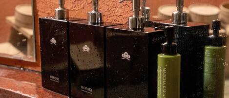 A bathroom with a mirror reflecting a row of black toiletries dispensers labeled "Hinoki".