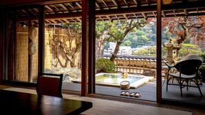 A traditional Japanese room with tatami flooring, a low table, and a view of a garden with a koi pond and a bonsai tree. - Wakamatsu HakoneYugawara (Yugawara)