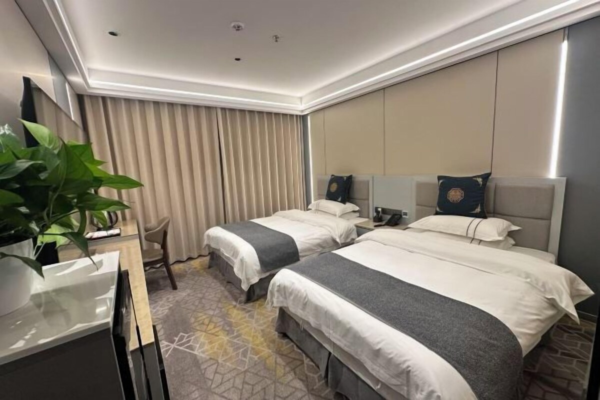 Una habitación de hotel con dos camas, un escritorio, una silla y una planta grande en maceta.