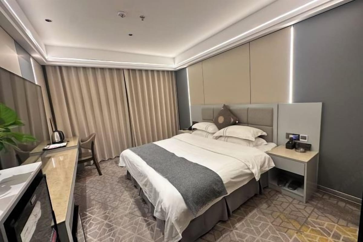Una habitación de hotel con cama, mesita de noche, escritorio y cortinas.